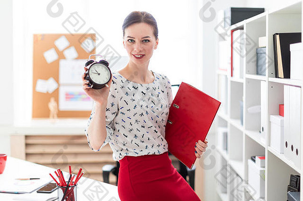 年轻的女孩站办公室持有红色的文件夹文档报警时钟
