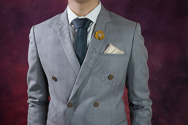 身穿双排扣灰色西装、格子图案、蓝色领带、花朵胸针和点图案手帕的男士，特写