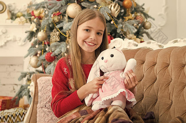 融化了心孩子玩软玩具女孩可爱的兔子圣诞节树小女孩持有兔子玩具小孩子快乐微笑现在圣诞节玩具