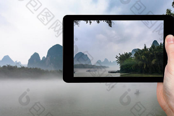 旅游理念——游客在平板电脑上拍摄中国阳朔县兴平镇附近河流上的雾气