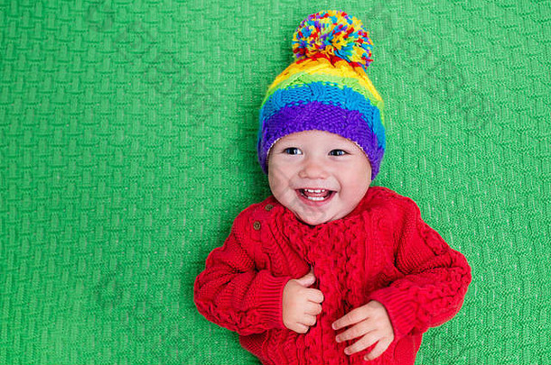 可爱的婴儿戴着温暖的羊毛针织帽，戴着红色毯子。儿童秋<strong>冬服装</strong>。彩色儿童针织品。