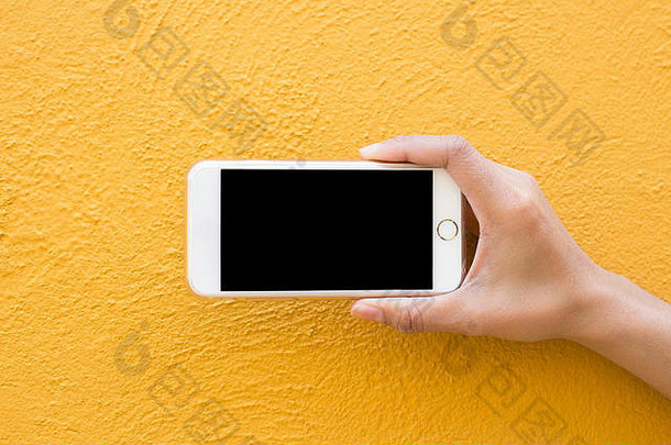 黄色墙壁背景上的手持白色智能手机