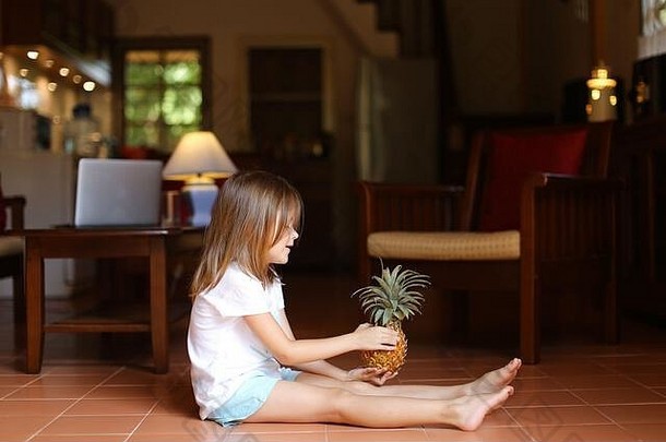 小女孩坐在地板上玩<strong>菠萝</strong>。
