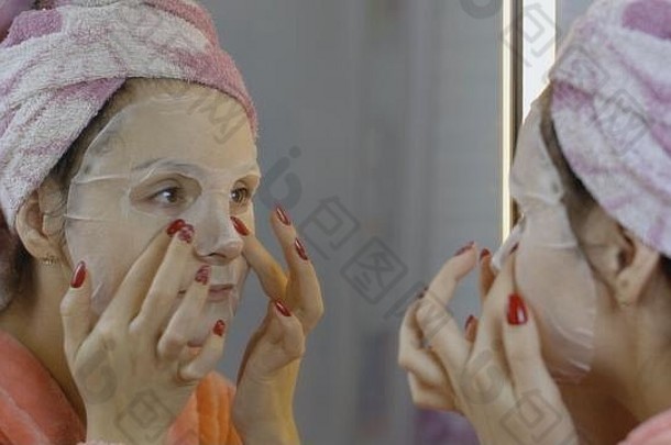 女人在浴室里戴着化妆面罩，看着镜子。照顾脸部皮肤的女孩。护肤水疗。面膜