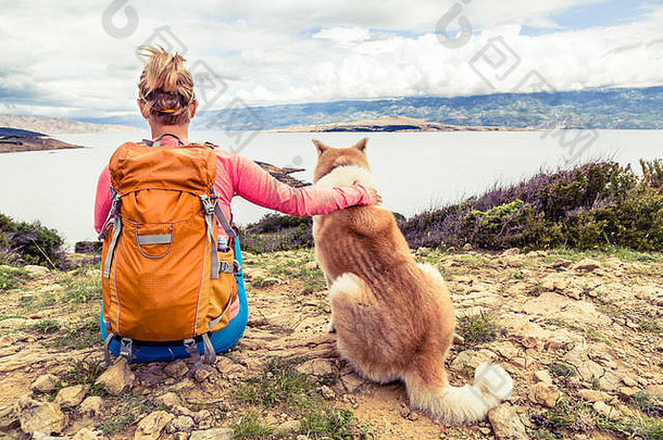 在海边的小径上，一名女子徒步旅行者和秋田犬一起看海。夏季山区户外休闲与健康生活方式