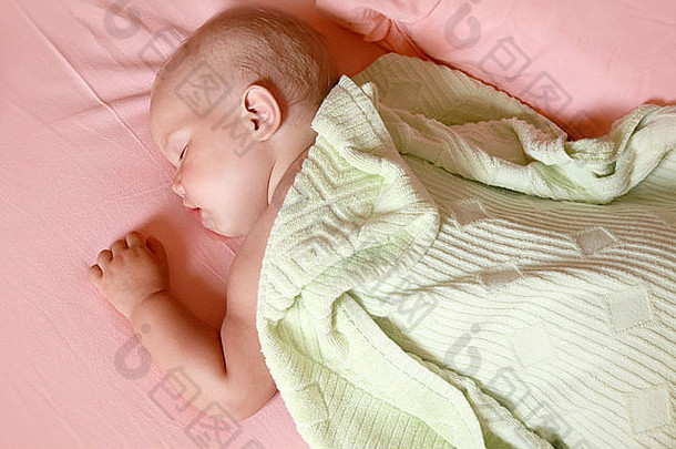 小婴儿睡在柔软的绿色毯子下的床上
