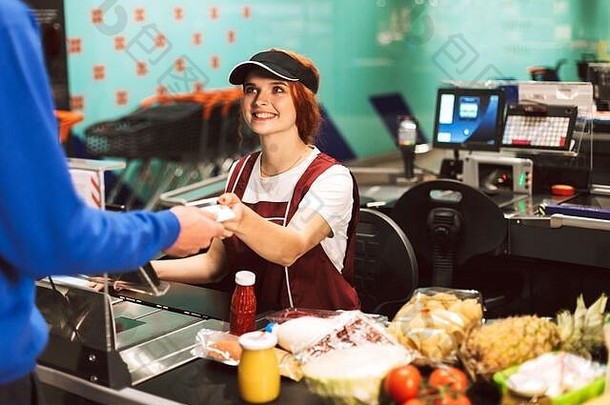 在现代超市工作时，身着制服、面带微笑的女收银员愉快地看着顾客