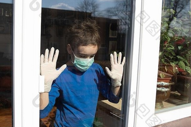 被隔离在家中的男孩戴着口罩，从关闭的窗户向外张望，以<strong>保护自己</strong>免受n-cov19冠状病毒大流行的影响