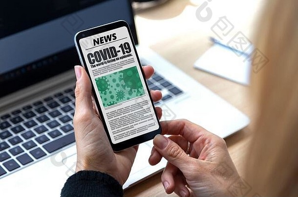 冠状病毒新闻。女人手里拿着2019冠状病毒疾病的智能手机。在屏幕上显示在线报纸页面。突发新闻。