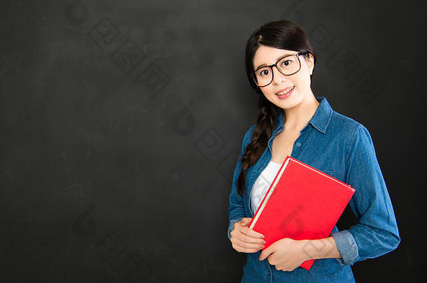 聪明的亚洲学生拿着一本书站在黑板前微笑着