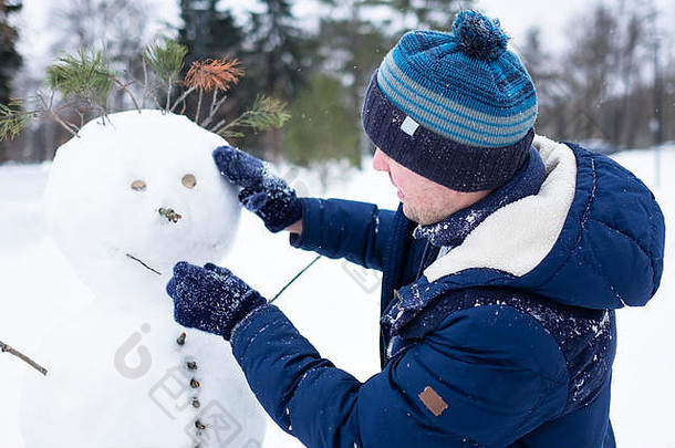 穿着暖和衣服的欧洲年轻人在户外用雪堆雪人。像孩子一样享受寒假的乐趣。