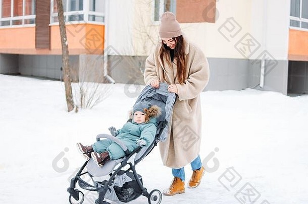 在冬天的街道上，一位年轻的母亲带着一个婴儿，坐在婴儿车里