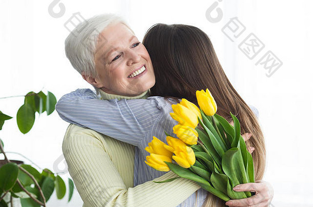年轻的女儿给花拥抱妈妈。首页