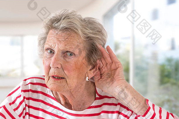 一位因年老而有听力问题的老太太手捂着耳朵，努力想听到声音。大窗户背景上的剖面图