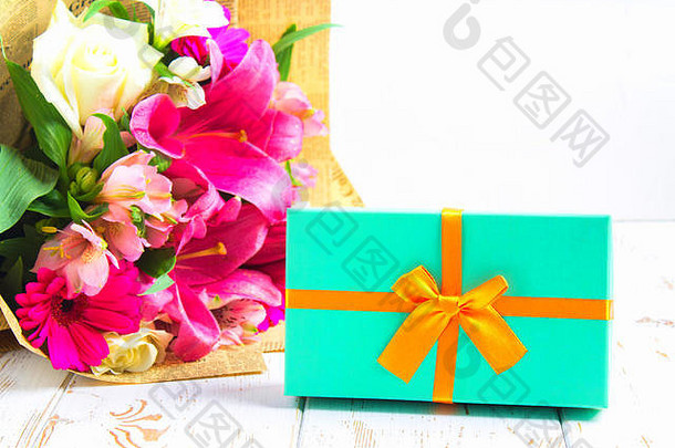 一个盒子里的礼物和一束花放在一张白色的木桌上。生日聚会。