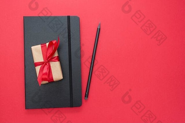 红色背景的黑色笔记本，带有礼品盒。情人节的概念。