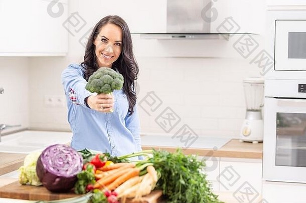 在厨房里拿着新鲜西兰花的顽皮的年轻女子——节食蔬菜和健康概念。