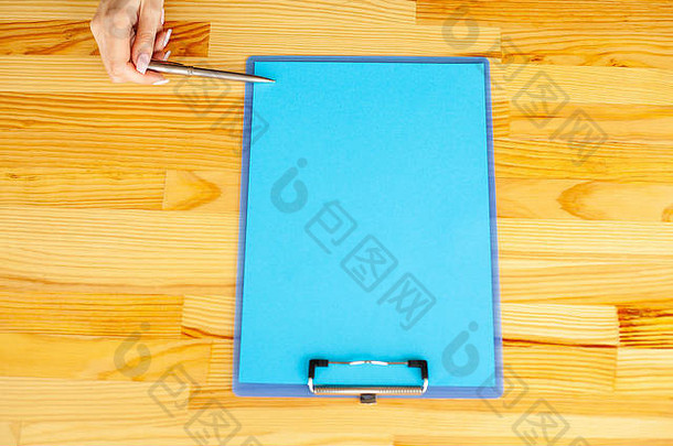 办公室里的一只手拿着一个文件夹，在木制桌子的彩色背景上放着一张蓝色的纸和笔。空间。放置文本