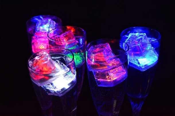 五个玻璃高脚杯在一条长长的扭曲的腿上，冰块以不同的颜色发光。配有发光led元件的有趣明亮的饮料。