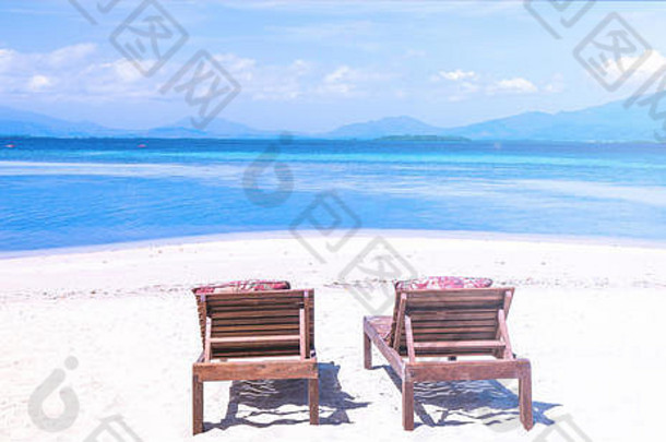 在蔚蓝的天空下，在海边美丽的沙滩上坐着椅子。暑期休闲的概念是一种旅游度假的理念。空拷贝空间