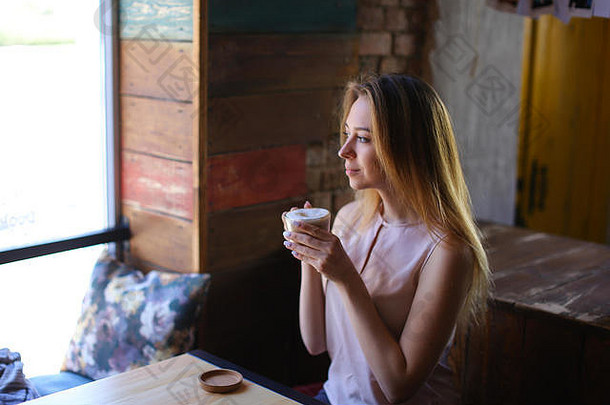 漂亮的女孩坐在桌子旁边，端着一杯咖啡，面带微笑。