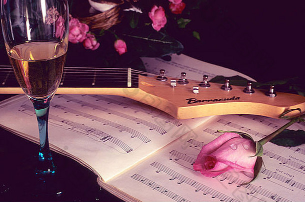 音乐书上粉红玫瑰的静物画，吉他和一杯酒