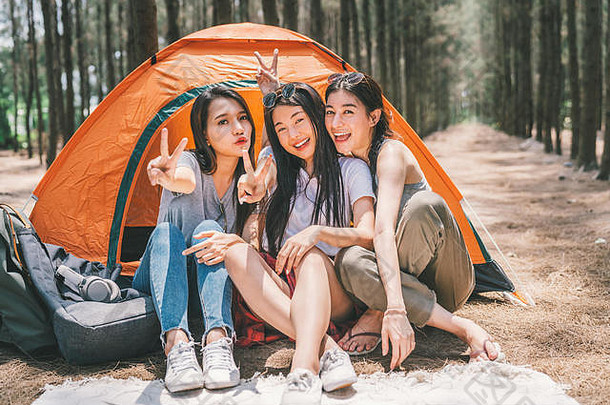 一群快乐的亚洲少女一起做着胜利的姿势，在帐篷旁露营。户外活动、探险旅行或度假概念