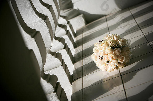 这是一个充满诗意的场景，一束美丽的圆形新娘象牙玫瑰放在铺着瓷砖的露台上，在一块经典的白色铸石的阴影下。。。
