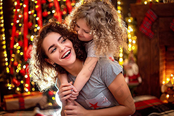 快乐可爱的卷发小女孩和她的姐姐在室内的圣诞树旁欢天喜地地拥抱着。在圣诞节房间里用礼物爱家人。