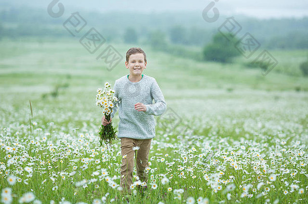 雨天和阳光下，一个微笑的男孩撑着雨伞，穿过野花丛生的草地，邓德里翁·甘菊雏菊，手里拿着花束