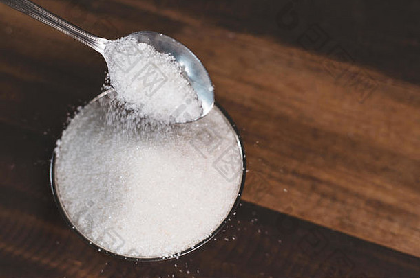 糖倒在木桌上的钢碗里。不健康饮食与糖尿病的概念