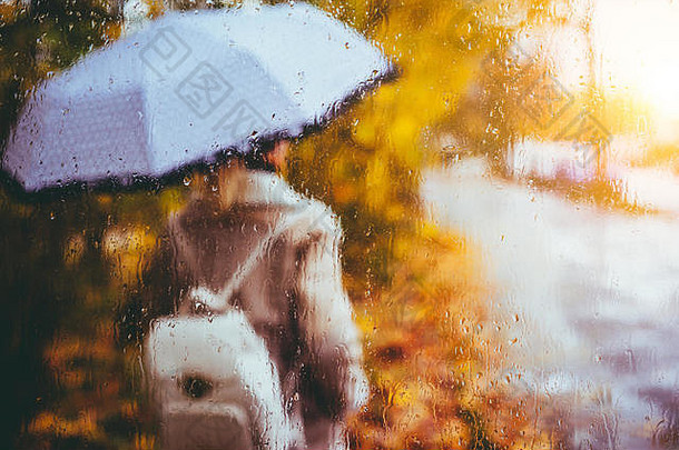 美丽的金秋季节。水彩般模糊的金发女孩背着背包，打着明亮的雨伞，站在雨滴下。背光夕阳光束在屏幕上闪烁。潮湿天气