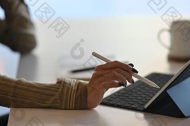 裁剪图像有创意的女人的手持有手写笔笔电脑平板电脑键盘情况下坐着白色工作桌子上