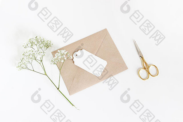 白色礼品标签，手工纸信封，金色剪刀和婴儿呼吸Gypsophila花隔离在白色桌面背景上。婚礼或生日风格的库存照片，俯视图，平面构成。