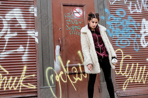 年轻漂亮时尚的少女站在城墙外，在禁烟区抽烟，满脸涂鸦