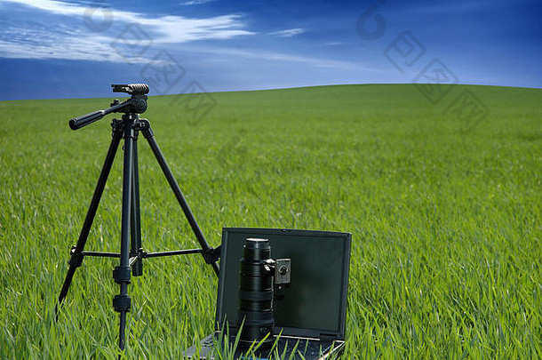摄影设备和笔记本电脑在绿色的田野上，蓝天白云背景下