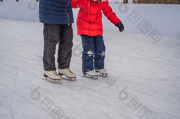年轻的母亲在室外溜冰场教她的小儿子滑冰。一家人在户外溜冰场上过冬