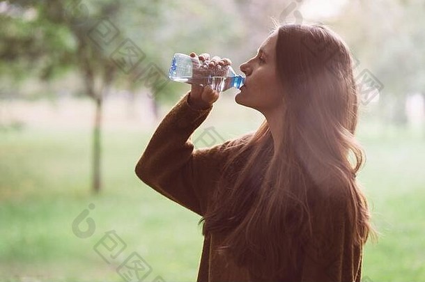 <strong>秋冬</strong>时<strong>节</strong>，在公园的街道上，年轻漂亮的女孩正在用塑料瓶喝水。一个留着漂亮又长又厚的黑头发的女人