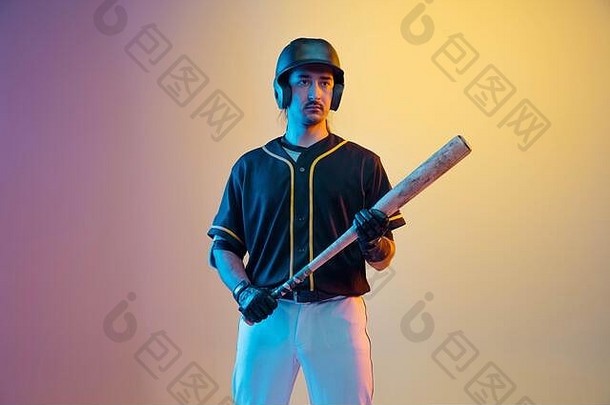棒球运动员，身穿黑色制服的投手，在霓虹灯的渐变背景下自信地摆出姿势。年轻的运动健将。健康的生活方式、运动、运动理念。