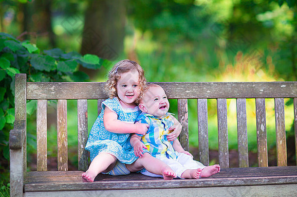 可爱的孩子们，<strong>小卷发</strong>女孩和可爱的，兄弟姐妹，一起坐在花园里的木凳上
