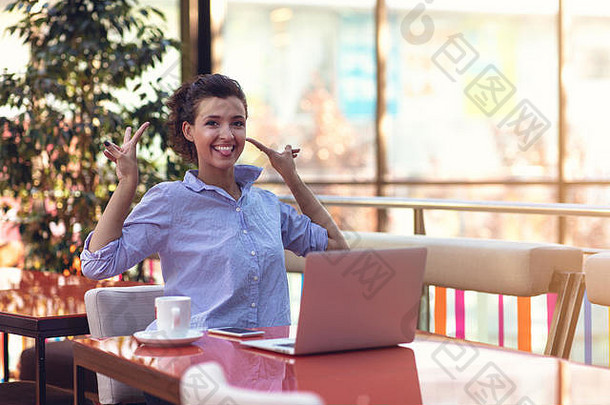 坐在咖啡馆里用笔记本电脑的快乐女人的照片。