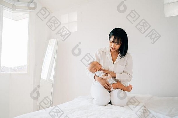 关怀的亚洲母亲双手抱着新生的儿子小宝宝睡在现代住宅的卧室里