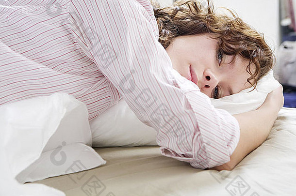 迷人体贴的黑发卷发女人，床上放着枕头。妇女问题