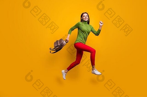 时髦漂亮的女士在学习后举着酷酷的年轻人包，穿着休闲的绿色套头衫红色长裤，跳得很高，冲回家