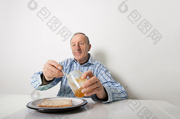 老人在餐桌上准备面包片和<strong>果酱</strong>的画像