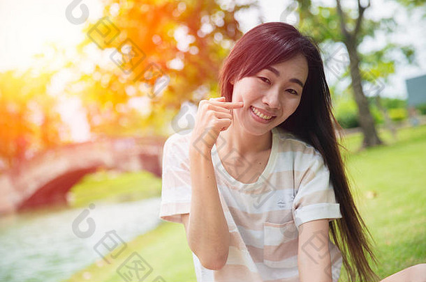 可爱的亚洲女人在公园里用手指酒窝笑着脸颊