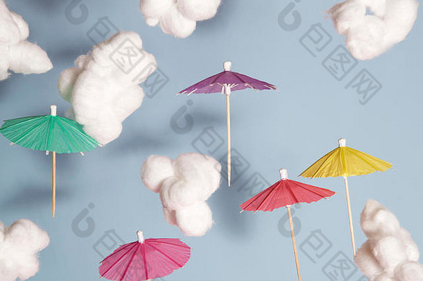 彩色鸡尾酒伞在空中飞舞，以棉花为云蓝色背景