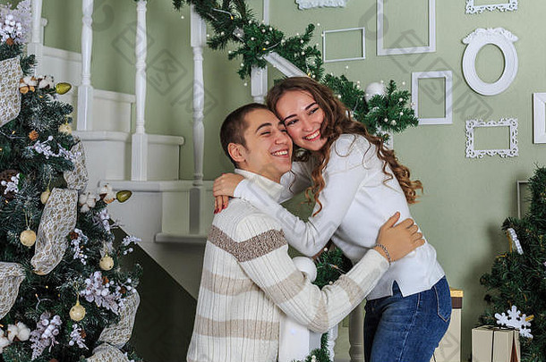 在圣诞节前夕，一对情侣站在房子的白色楼梯上互相拥抱。