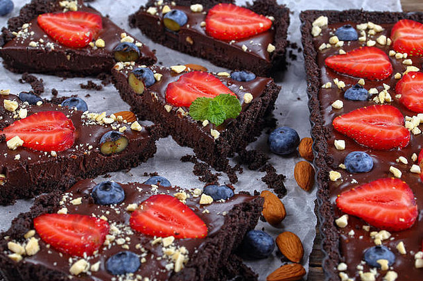 纸上有几片未烘焙的巧克力蛋糕馅饼，上面有新鲜的蓝莓、草莓、薄荷叶和切碎的杏仁