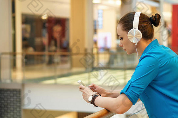 年轻的有吸引力的女孩听音乐耳机持有细胞电话站过渡购物中心